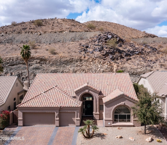 view of front of house with a tile roof, an attached garage, decorative driveway, a mountain view, and stucco siding