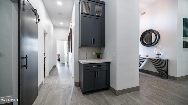 hall with a barn door, wood finish floors, visible vents, and baseboards