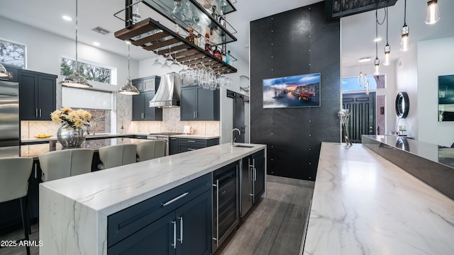 kitchen featuring visible vents, wine cooler, a sink, wall chimney range hood, and backsplash