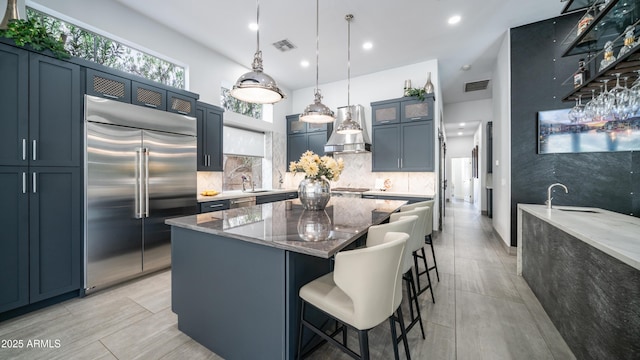 kitchen featuring visible vents, stainless steel built in refrigerator, light stone counters, and a kitchen breakfast bar