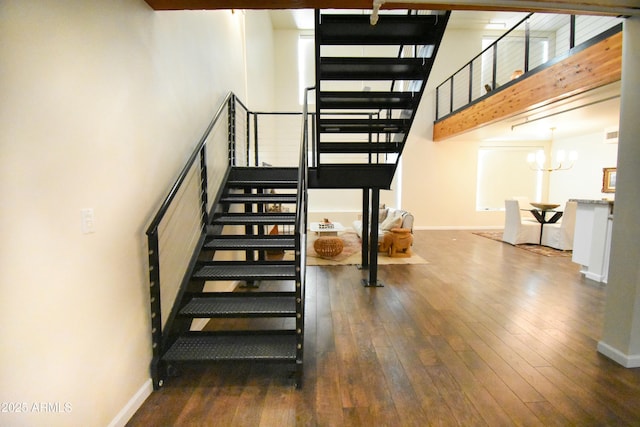 staircase with a towering ceiling, wood-type flooring, and a notable chandelier