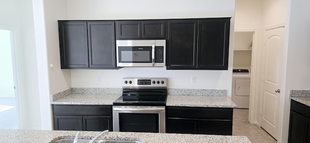 kitchen featuring sink, light stone countertops, appliances with stainless steel finishes, light tile patterned flooring, and washer / clothes dryer