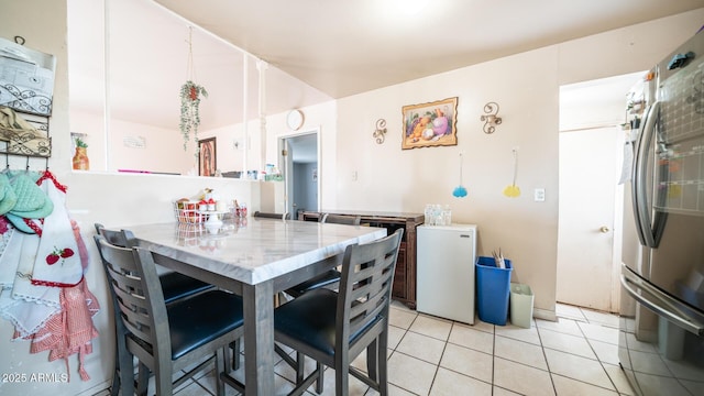 kitchen with stainless steel refrigerator, refrigerator, light stone countertops, and light tile patterned floors