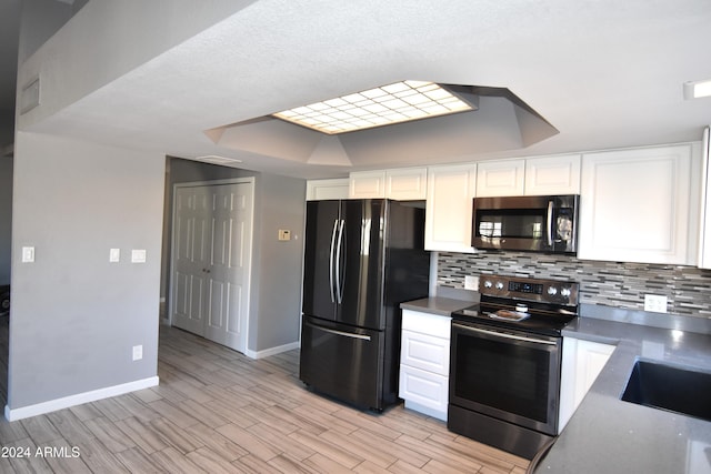 kitchen featuring white cabinets, appliances with stainless steel finishes, a tray ceiling, and decorative backsplash