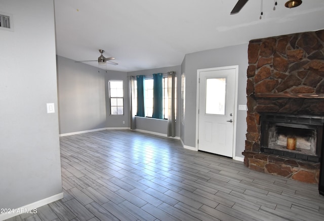 unfurnished living room with a stone fireplace and ceiling fan