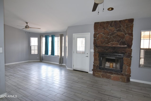 unfurnished living room with a stone fireplace, ceiling fan, and wood-type flooring