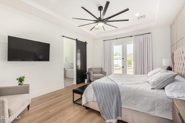 bedroom with access to exterior, a raised ceiling, ceiling fan, a barn door, and light hardwood / wood-style flooring