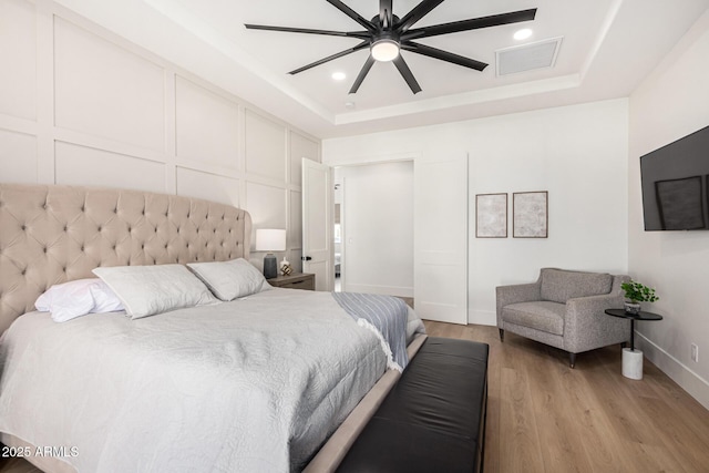 bedroom featuring ceiling fan, light hardwood / wood-style floors, and a tray ceiling