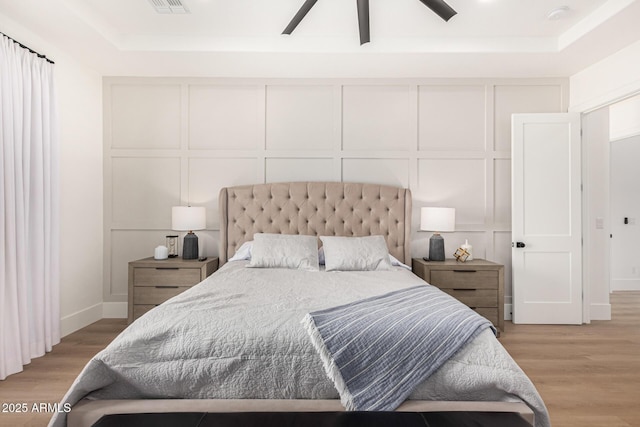 bedroom with ceiling fan, a raised ceiling, and light wood-type flooring