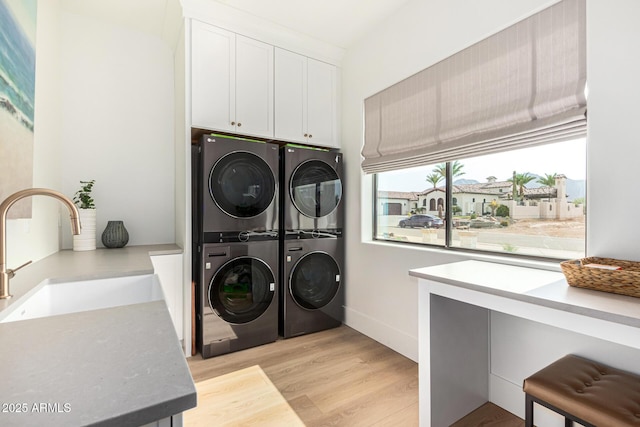 laundry area with cabinets, stacked washer and dryer, sink, and light wood-type flooring