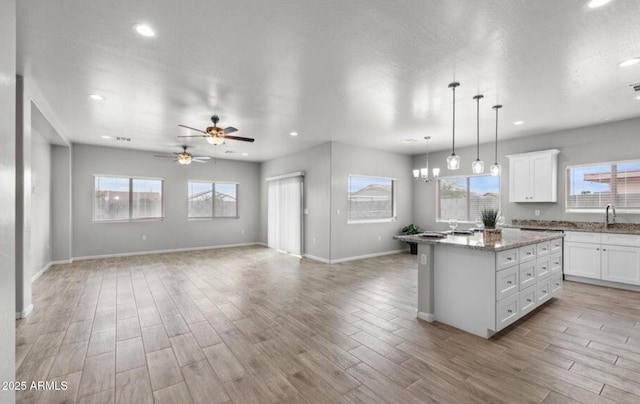 kitchen featuring white cabinetry, a center island, light hardwood / wood-style flooring, pendant lighting, and light stone countertops