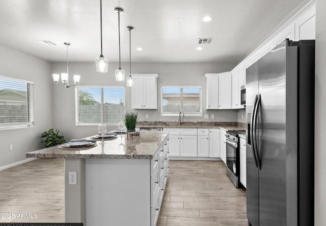 kitchen with appliances with stainless steel finishes, pendant lighting, white cabinetry, a center island, and light hardwood / wood-style flooring