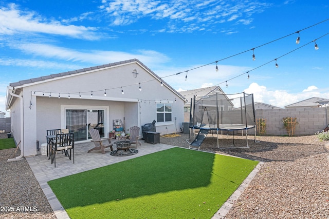 rear view of property with a patio, a yard, a fire pit, and a trampoline