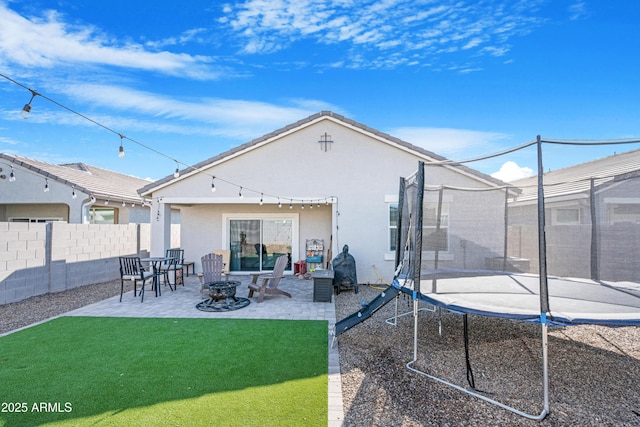 rear view of house featuring a patio, a lawn, a trampoline, and an outdoor fire pit