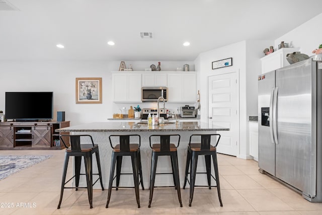 kitchen with stainless steel appliances, a center island with sink, white cabinets, and dark stone counters