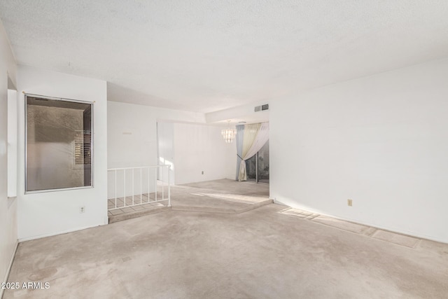 unfurnished room with visible vents, a notable chandelier, and a textured ceiling