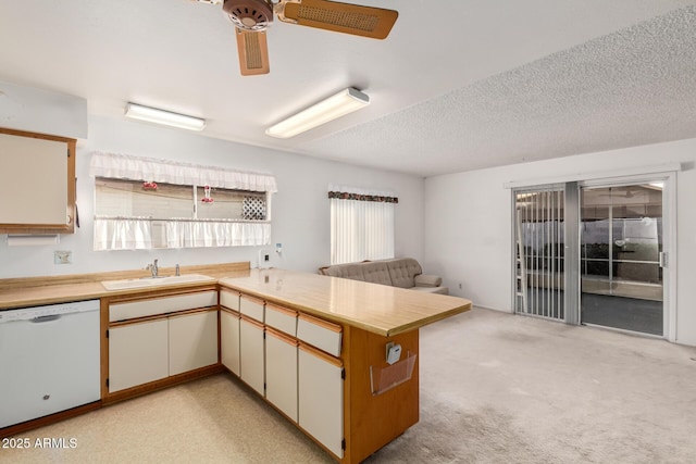 kitchen with a peninsula, a sink, open floor plan, light countertops, and dishwasher