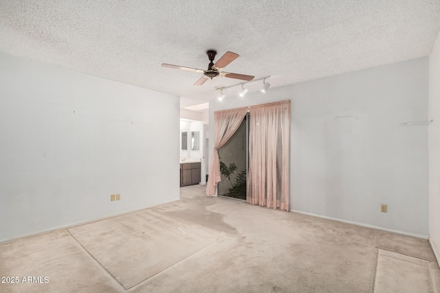 unfurnished room with a textured ceiling, light carpet, a ceiling fan, baseboards, and rail lighting