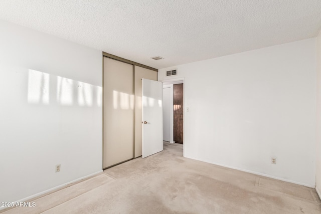 unfurnished bedroom with a closet, visible vents, light carpet, a textured ceiling, and baseboards