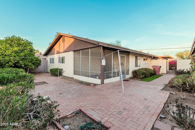 back of house featuring a sunroom, a patio area, fence, and a gate