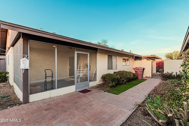 view of front of property featuring a sunroom, stucco siding, fence, and a gate