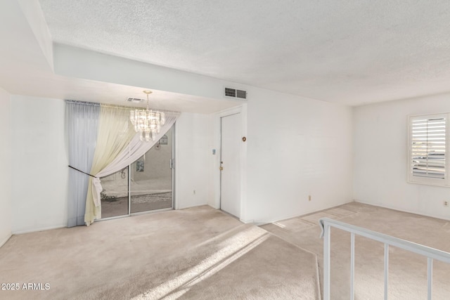 carpeted spare room featuring an inviting chandelier, visible vents, and a textured ceiling