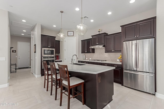 kitchen with an island with sink, stainless steel appliances, pendant lighting, a breakfast bar, and sink