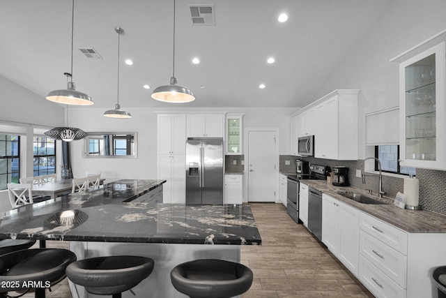 kitchen with appliances with stainless steel finishes, a spacious island, sink, decorative light fixtures, and dark stone countertops