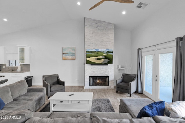 living room featuring ceiling fan, a fireplace, high vaulted ceiling, and light wood-type flooring