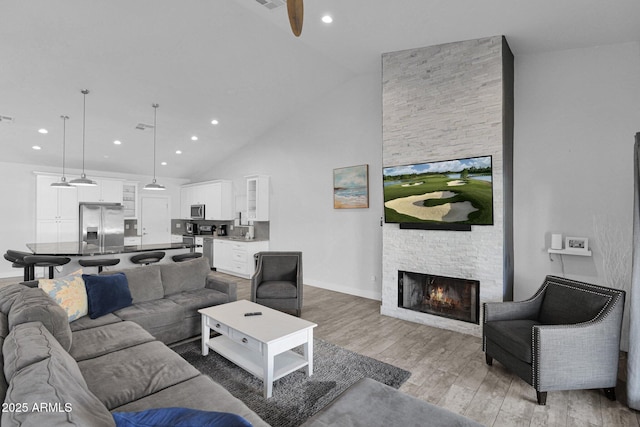 living room featuring ceiling fan, a stone fireplace, light wood-type flooring, and high vaulted ceiling