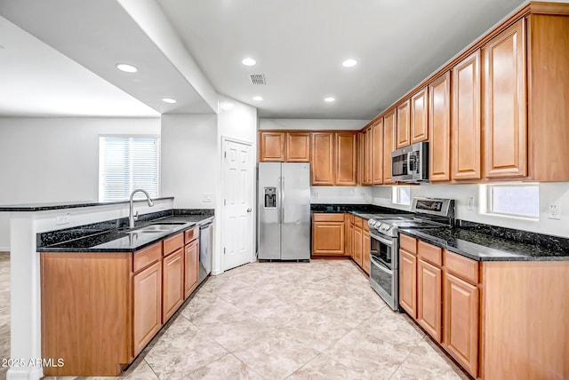 kitchen featuring visible vents, appliances with stainless steel finishes, dark stone countertops, a peninsula, and a sink