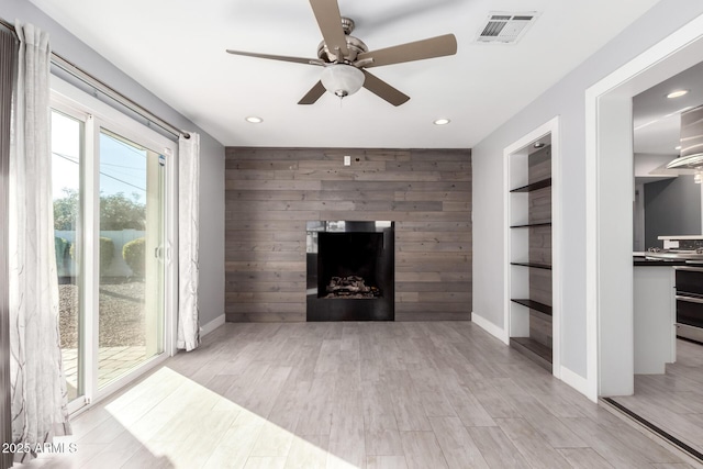 unfurnished living room with ceiling fan, wooden walls, built in features, and light wood-type flooring