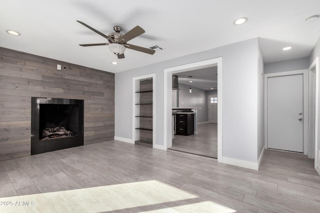 unfurnished living room with ceiling fan, light hardwood / wood-style floors, and wood walls