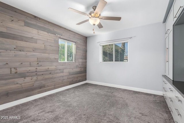 spare room featuring dark colored carpet, ceiling fan, and wooden walls