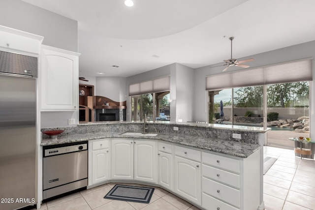 kitchen with white cabinets, stainless steel appliances, sink, kitchen peninsula, and light stone counters