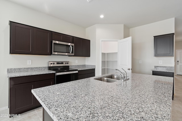 kitchen featuring appliances with stainless steel finishes, light stone counters, dark brown cabinetry, and sink