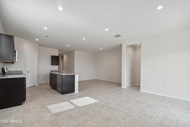 kitchen with light tile patterned floors, a kitchen island with sink, light stone counters, and range