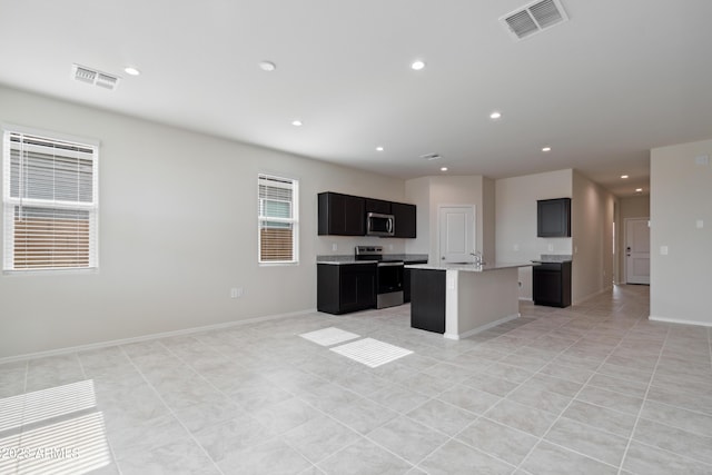 kitchen with light tile patterned floors, appliances with stainless steel finishes, and an island with sink