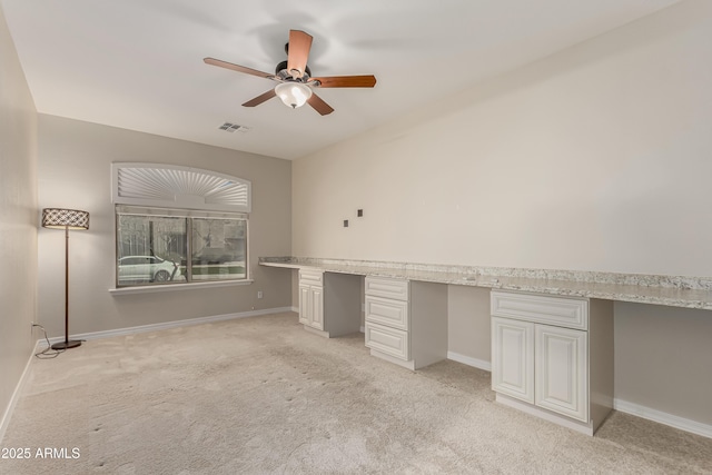 unfurnished office featuring ceiling fan, built in desk, and light carpet