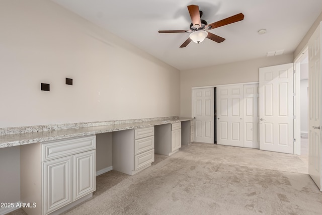 unfurnished office featuring ceiling fan, light colored carpet, and built in desk