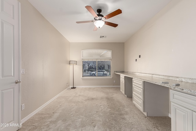 interior space with white cabinetry, light stone counters, built in desk, light carpet, and ceiling fan