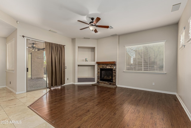 unfurnished living room with ceiling fan, a stone fireplace, built in features, and light wood-type flooring