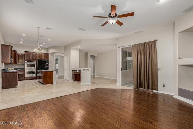 kitchen with an island with sink, hanging light fixtures, ceiling fan, dark brown cabinetry, and light hardwood / wood-style floors