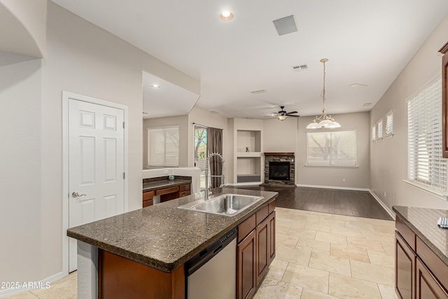 kitchen featuring pendant lighting, a kitchen island with sink, a wealth of natural light, a stone fireplace, and stainless steel dishwasher