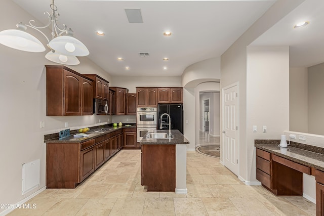 kitchen with a kitchen island with sink, dark stone countertops, dark brown cabinets, stainless steel appliances, and decorative light fixtures