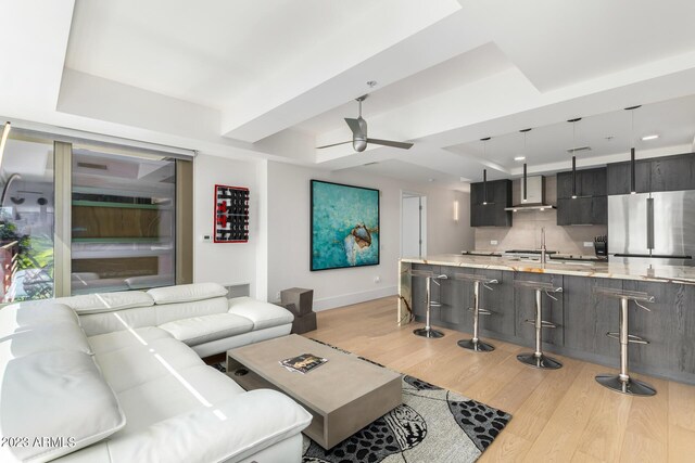 living room featuring ceiling fan, light hardwood / wood-style floors, and a tray ceiling