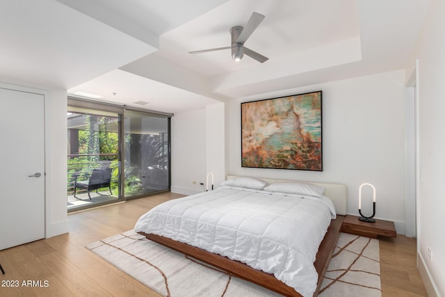 bedroom featuring expansive windows, access to outside, ceiling fan, a tray ceiling, and light hardwood / wood-style flooring