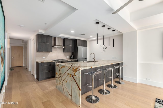 kitchen featuring wall chimney exhaust hood, sink, light hardwood / wood-style flooring, built in fridge, and pendant lighting