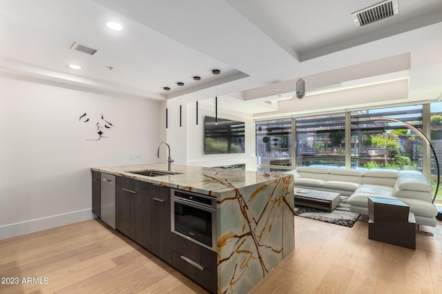 kitchen with dark brown cabinets, sink, wall oven, and light hardwood / wood-style floors