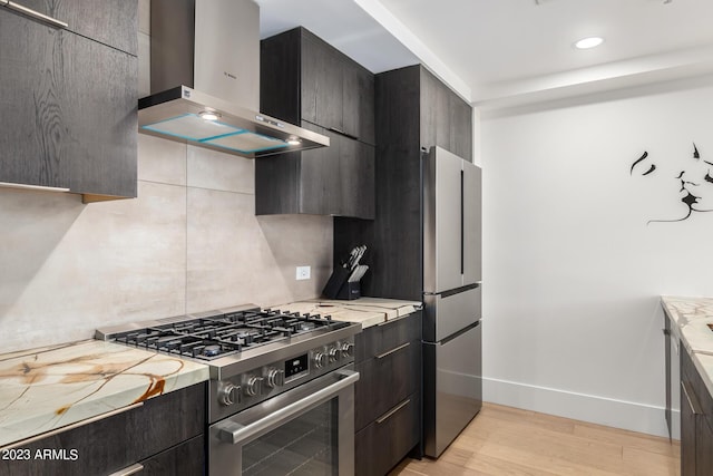 kitchen featuring wall chimney range hood, stainless steel appliances, light stone countertops, light hardwood / wood-style floors, and backsplash